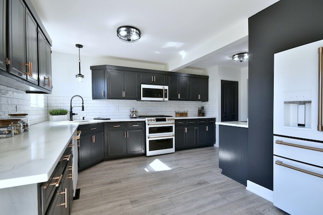 kitchen featuring backsplash, decorative light fixtures, light wood-type flooring, range with two ovens, and a sink