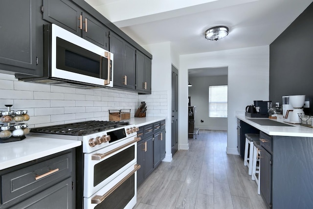 kitchen featuring light wood-style flooring, tasteful backsplash, white appliances, light countertops, and baseboards