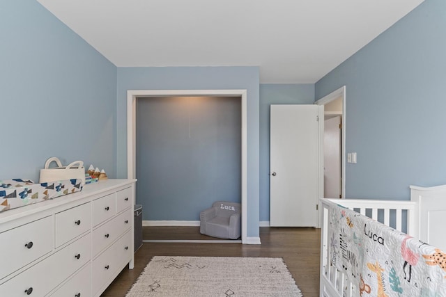 bedroom featuring a nursery area, baseboards, and dark wood-style flooring