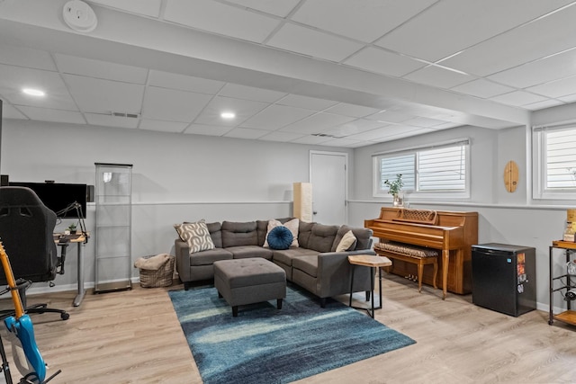 living area with visible vents, baseboards, light wood-style floors, and a drop ceiling