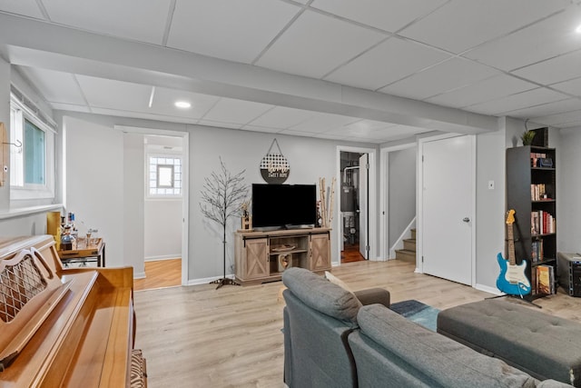 living room featuring a drop ceiling, stairs, and light wood-style floors