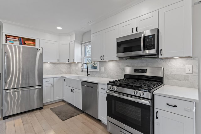 kitchen featuring light countertops, decorative backsplash, stainless steel appliances, white cabinetry, and a sink