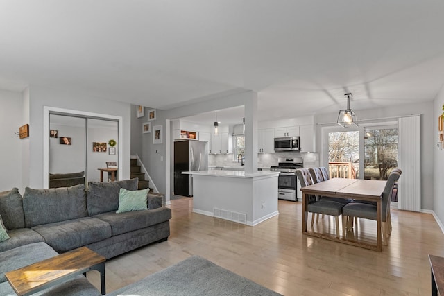 living area featuring visible vents, light wood-style flooring, stairs, and baseboards