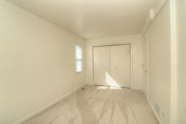 unfurnished bedroom featuring visible vents, baseboards, light colored carpet, and a closet