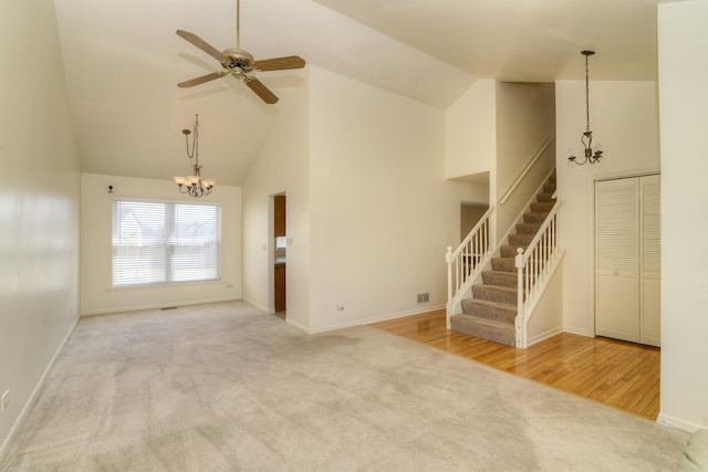 unfurnished living room featuring baseboards, stairway, carpet flooring, ceiling fan with notable chandelier, and high vaulted ceiling