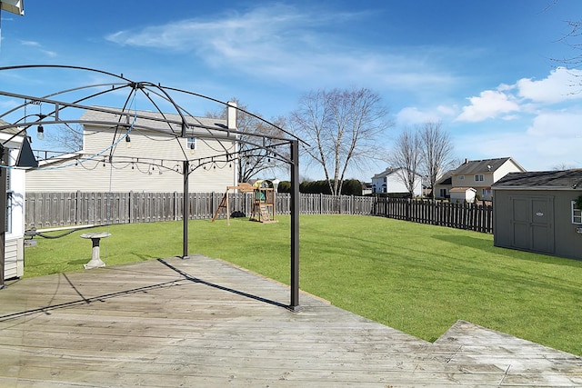 view of yard featuring a playground, a shed, a wooden deck, a fenced backyard, and an outbuilding