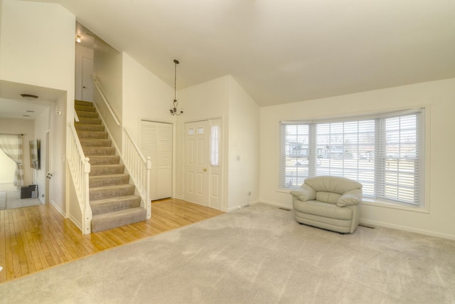 carpeted foyer entrance featuring a chandelier, high vaulted ceiling, stairs, and baseboards