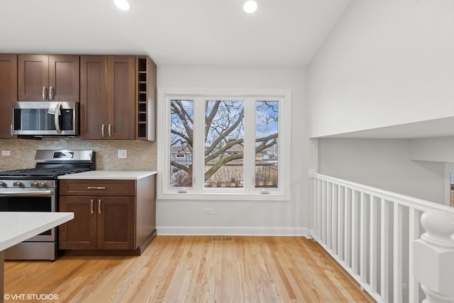 kitchen with baseboards, decorative backsplash, light countertops, appliances with stainless steel finishes, and light wood-type flooring