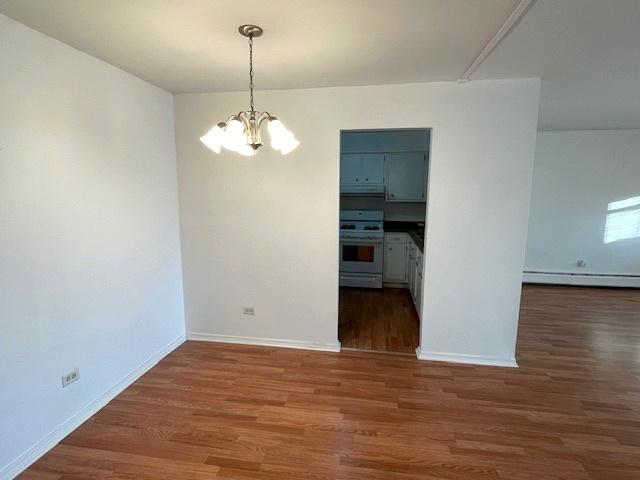 unfurnished dining area with a baseboard heating unit, an inviting chandelier, wood finished floors, and baseboards