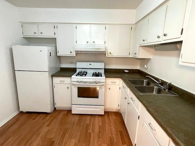 kitchen featuring dark countertops, under cabinet range hood, wood finished floors, white appliances, and a sink