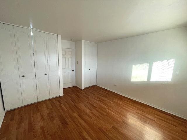 unfurnished bedroom with baseboards, multiple closets, and wood finished floors