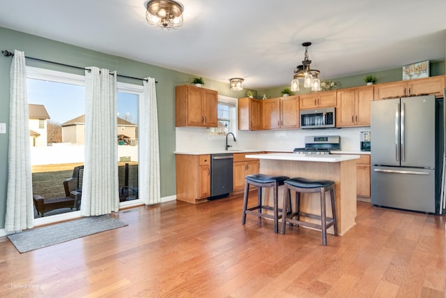 kitchen featuring a breakfast bar, a center island, stainless steel appliances, light wood-style floors, and light countertops