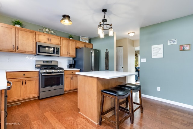 kitchen featuring baseboards, stainless steel appliances, light countertops, light wood-style floors, and a kitchen bar