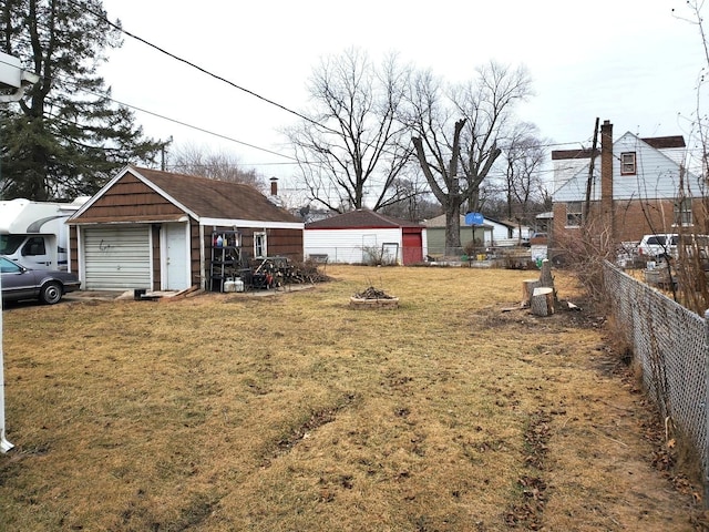 view of yard with an outbuilding, an outdoor fire pit, a detached garage, and fence