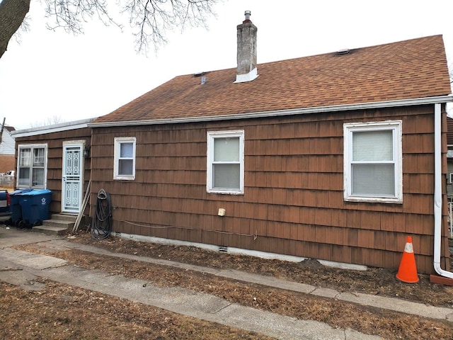 view of property exterior with a chimney, entry steps, and a shingled roof