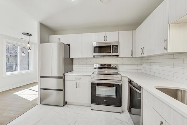 kitchen featuring marble finish floor, decorative light fixtures, backsplash, appliances with stainless steel finishes, and light countertops