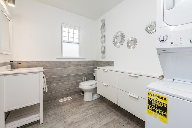 bathroom with toilet, wainscoting, stacked washer and clothes dryer, wood finished floors, and vanity