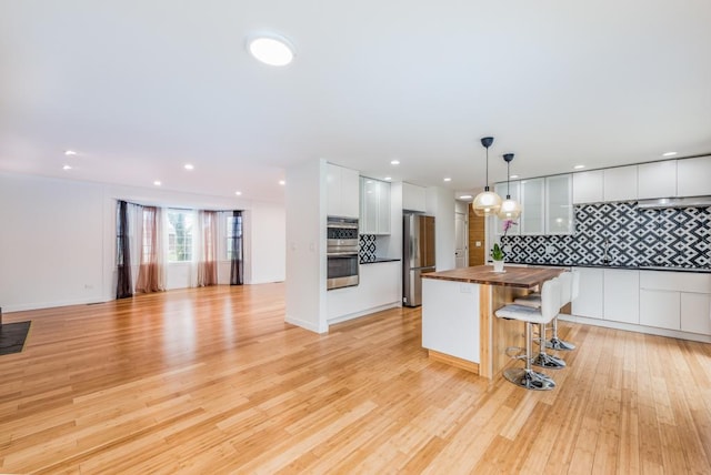 kitchen featuring light wood-style flooring, wood counters, tasteful backsplash, white cabinetry, and appliances with stainless steel finishes