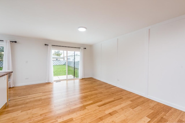 empty room with light wood-type flooring, baseboards, and a decorative wall