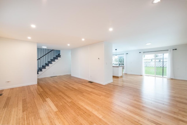 unfurnished living room with stairway, recessed lighting, light wood-style floors, and baseboards