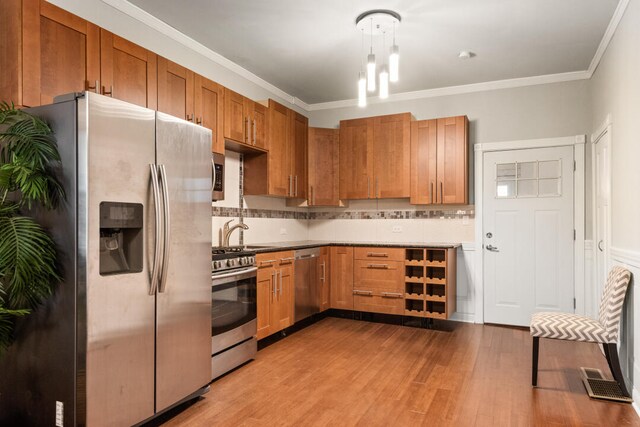 kitchen with wood finished floors, stainless steel appliances, brown cabinetry, crown molding, and decorative backsplash