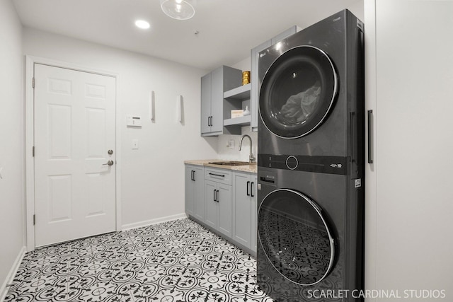laundry area with cabinet space, a sink, recessed lighting, baseboards, and stacked washer / dryer