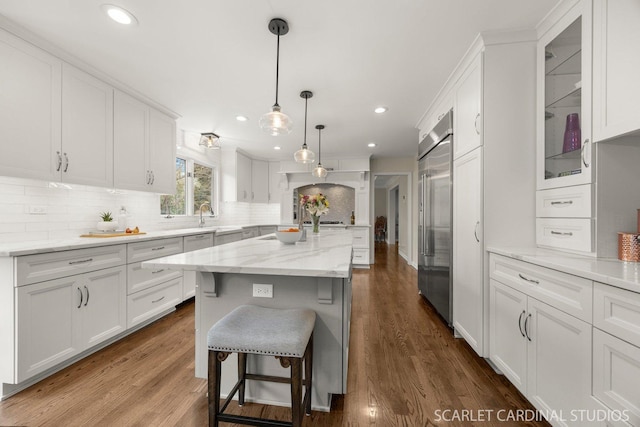 kitchen with glass insert cabinets, a kitchen breakfast bar, white cabinets, built in fridge, and backsplash