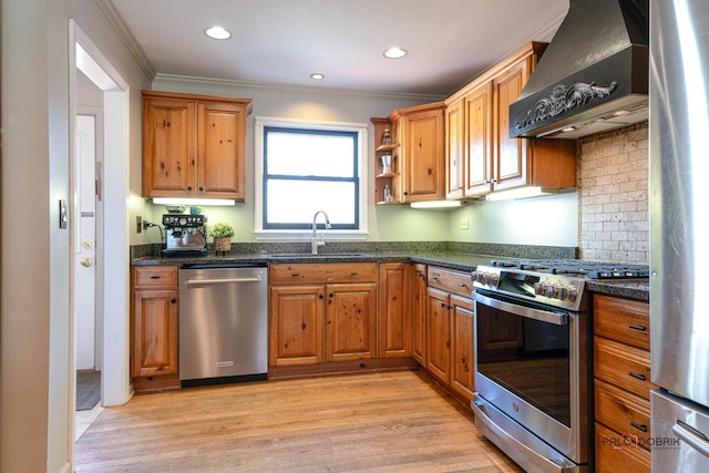 kitchen featuring light wood-type flooring, a sink, appliances with stainless steel finishes, wall chimney exhaust hood, and crown molding