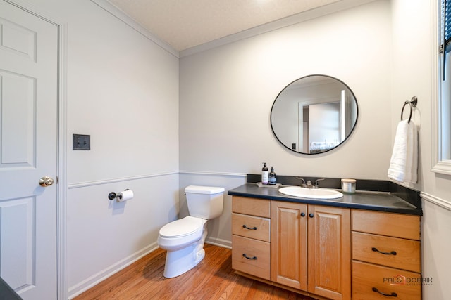 bathroom featuring toilet, wood finished floors, crown molding, baseboards, and vanity