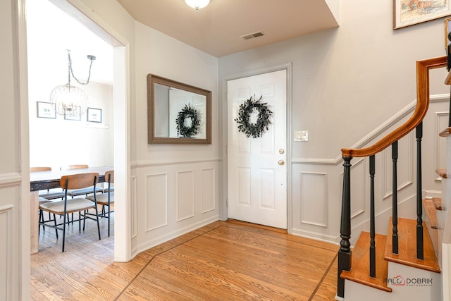 foyer with stairway, visible vents, light wood finished floors, an inviting chandelier, and a decorative wall