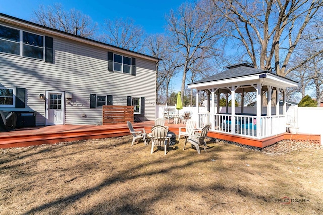 back of property with fence, an outdoor fire pit, a wooden deck, a gazebo, and a lawn