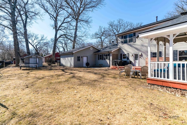 back of house with an outdoor structure, a trampoline, a lawn, and fence