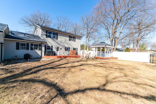 rear view of property featuring a gazebo, a yard, a wooden deck, and fence