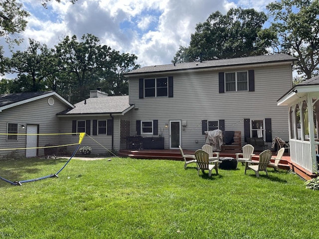 rear view of house featuring a lawn, a chimney, a deck, and roof with shingles