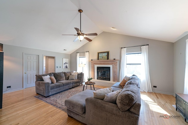 living room featuring lofted ceiling, a ceiling fan, a glass covered fireplace, light wood finished floors, and baseboards