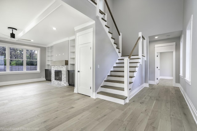 unfurnished living room with a stone fireplace, stairway, baseboards, and light wood-style floors