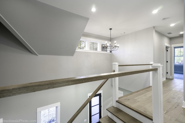 staircase featuring wood finished floors, a notable chandelier, recessed lighting, and visible vents