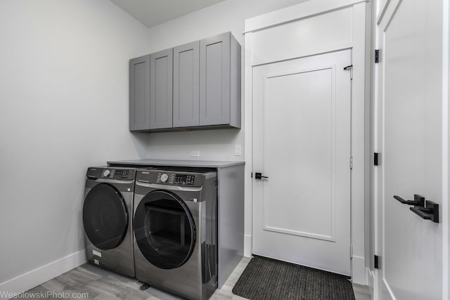 laundry room featuring washer and dryer, cabinet space, baseboards, and light wood finished floors