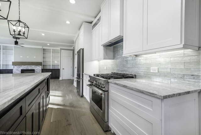 kitchen with under cabinet range hood, a glass covered fireplace, light wood-style floors, appliances with stainless steel finishes, and white cabinets