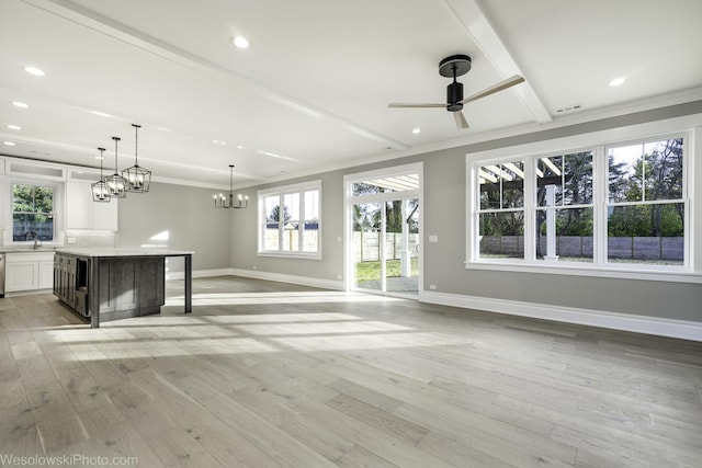 unfurnished living room with light wood-style flooring, ceiling fan with notable chandelier, baseboards, and a sink