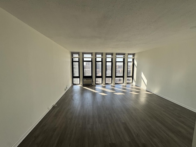 empty room featuring a textured ceiling, baseboards, dark wood-style flooring, and expansive windows