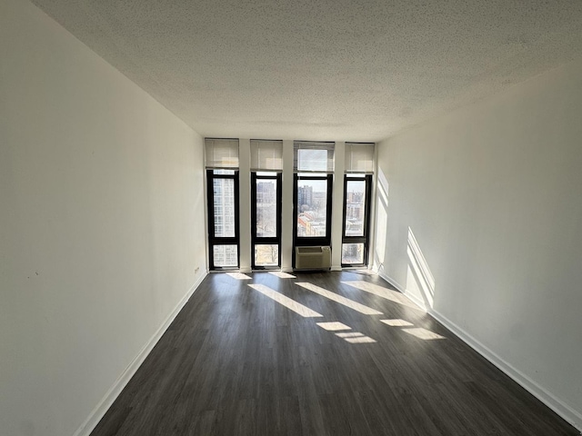 empty room featuring expansive windows, baseboards, dark wood-type flooring, and a textured ceiling