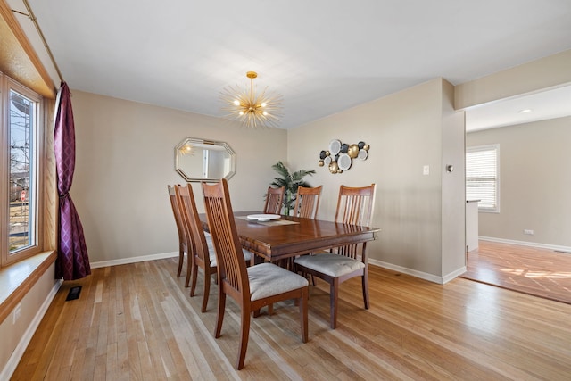 dining area featuring light wood-style flooring, a notable chandelier, and baseboards