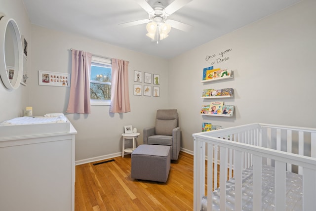 bedroom featuring baseboards, a crib, visible vents, and light wood finished floors