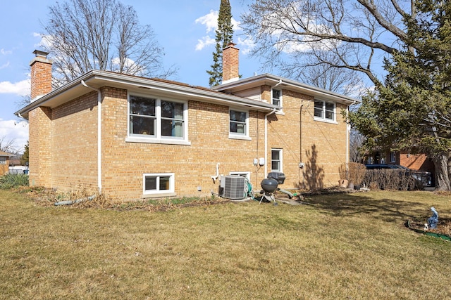 rear view of property with a yard, brick siding, central AC, and a chimney