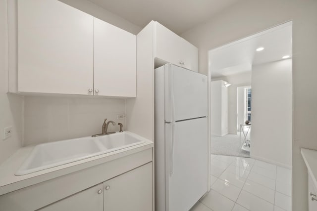 kitchen featuring light countertops, white cabinets, freestanding refrigerator, and a sink