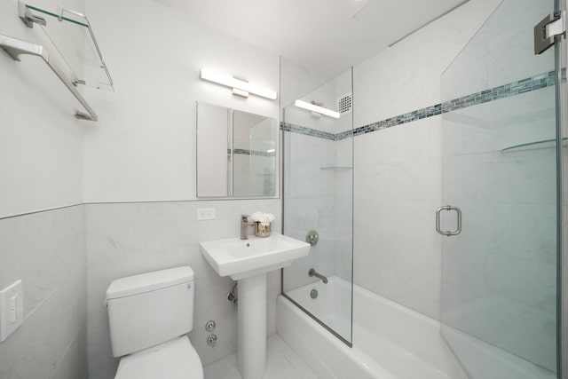 bathroom featuring a sink, toilet, tile walls, and shower / bath combination with glass door