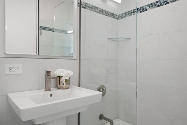 bathroom with tile walls, walk in shower, and a sink