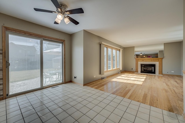 unfurnished living room with visible vents, a ceiling fan, light tile patterned floors, baseboards, and a tile fireplace