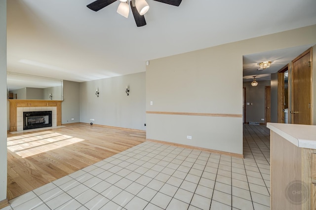 unfurnished living room with ceiling fan, baseboards, light tile patterned flooring, and a tile fireplace